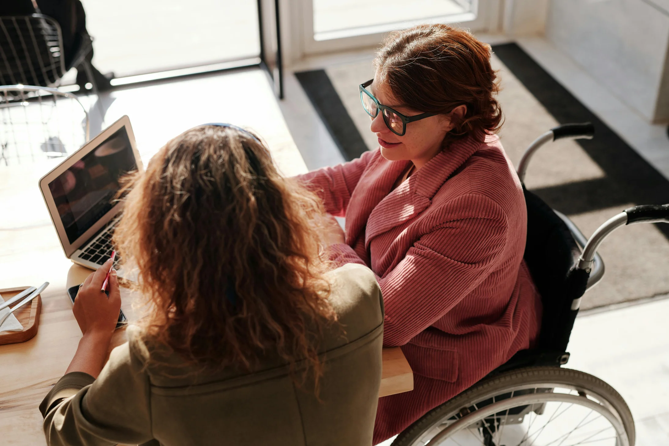 Woman in red sweater wearing black framed eyeglasses sitting on wheelchair