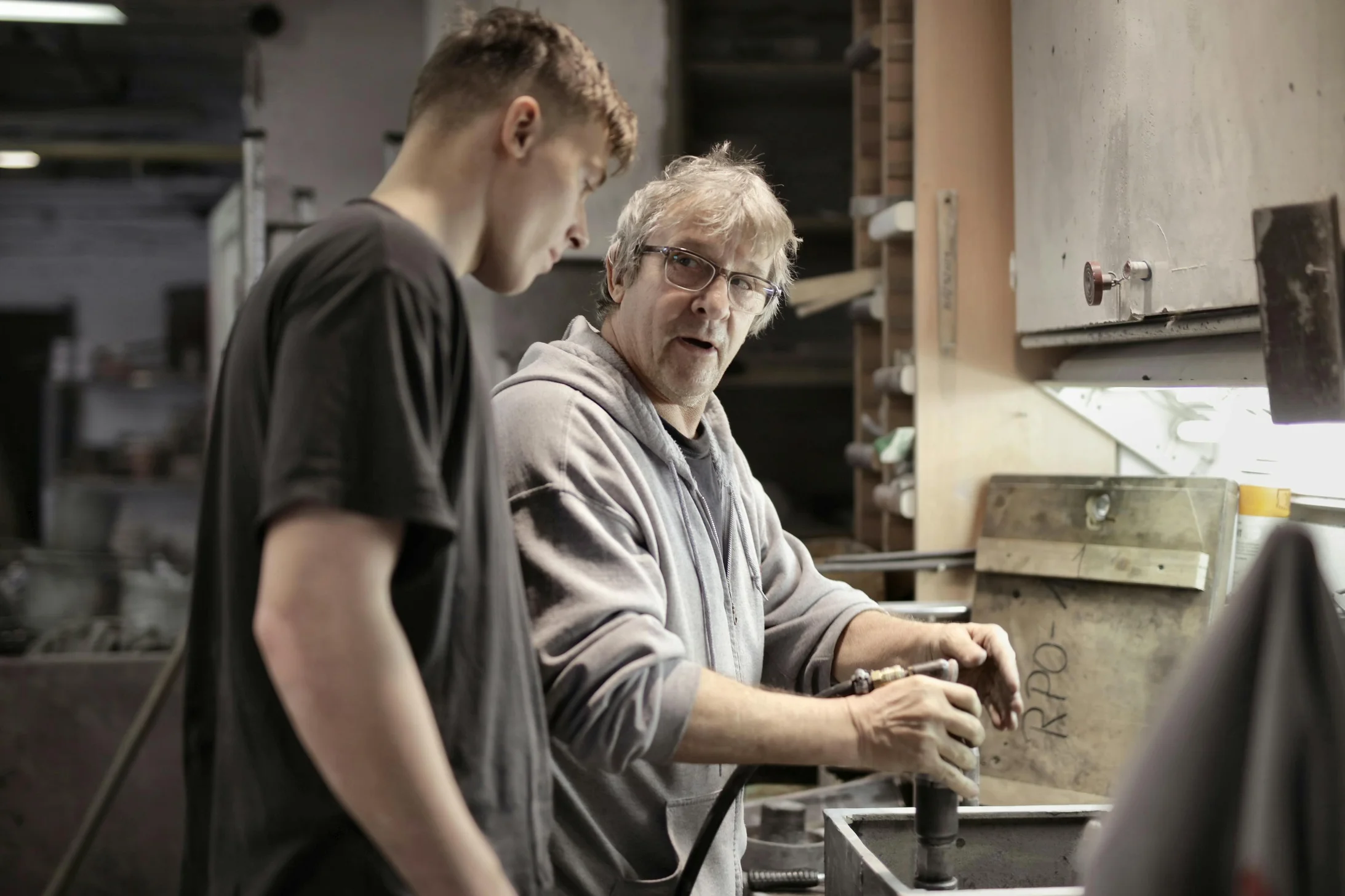 Workers handling detail by pneumatic tool in workshop